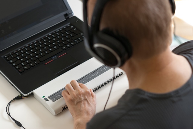 Un homme aveugle utilise une plage braille pour son ordinateur avec un casque sur la tête pour la synthèse vocale